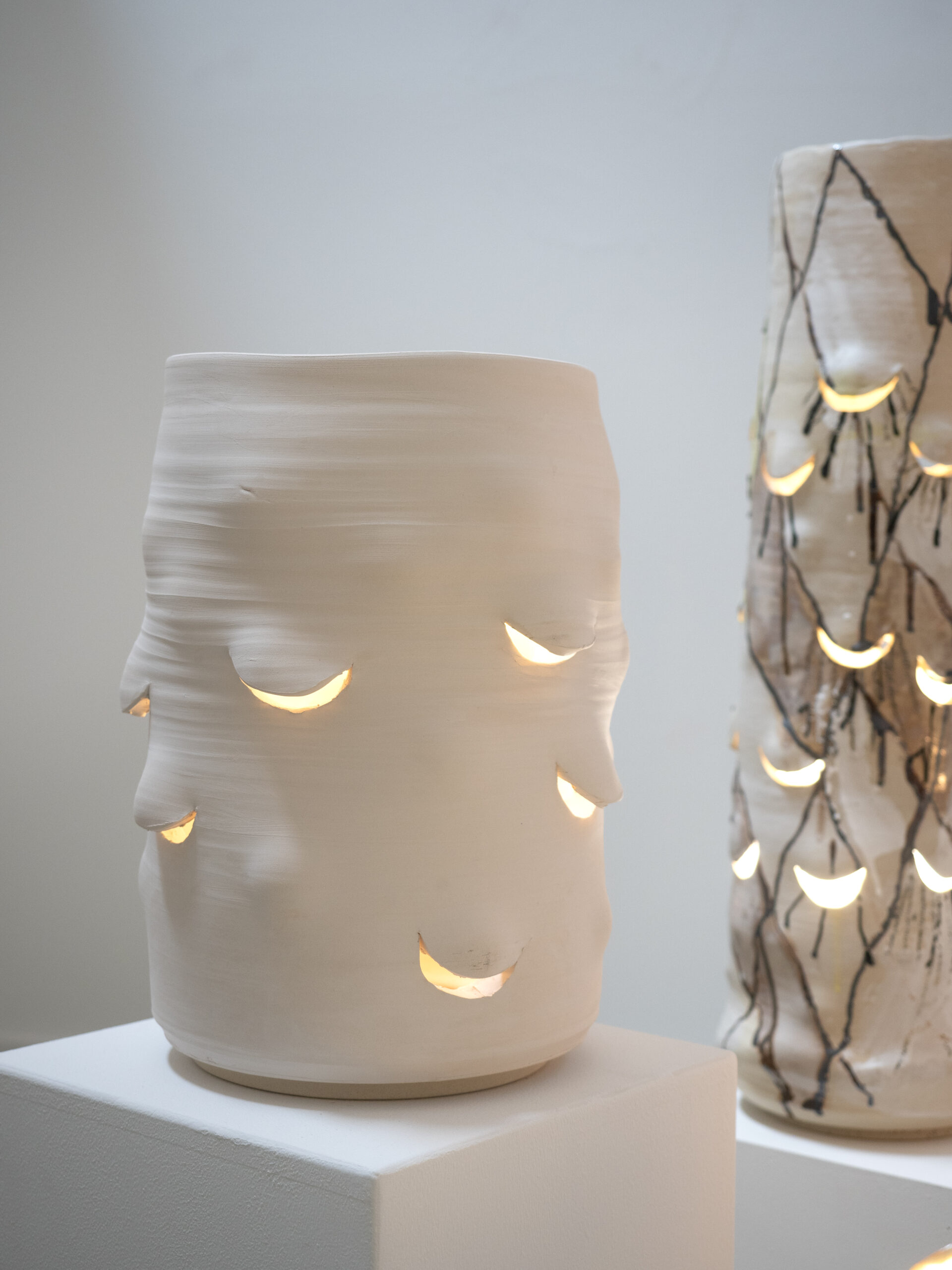 Large white stoneware light sculpture with half-closed eyes and visible hand-formed textures, illuminated from within.