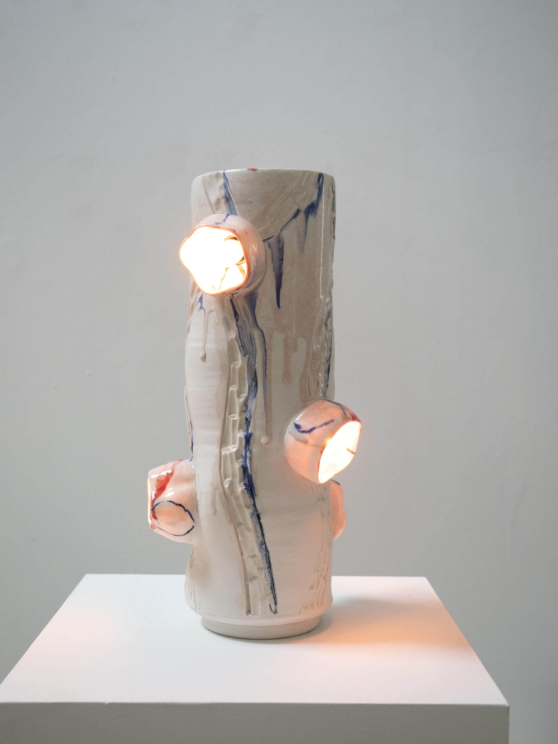 Porcelain light sculpture with five delicate flower forms emerging from a hand-shaped cylinder, illuminated by warm light.
